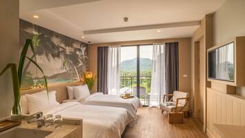 Une chambre d’hôtel avec deux lits, une télévision, un balcon donnant sur les montagnes et un tableau représentant une scène de plage.
