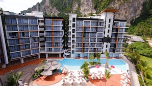 Un hotel de varios pisos, con piscina y montañas al fondo.