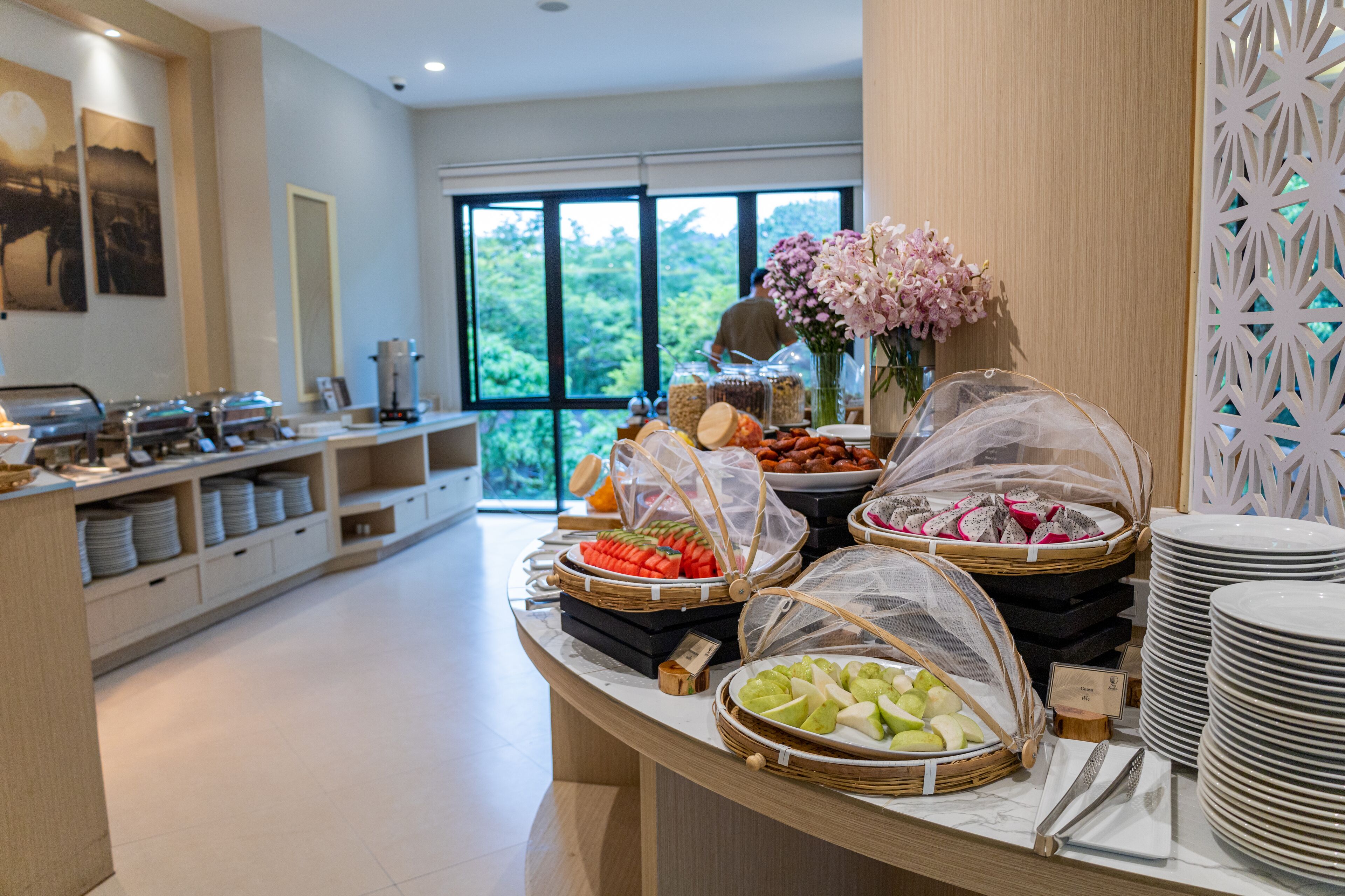 A buffet setup with various food items and a view of greenery outside.