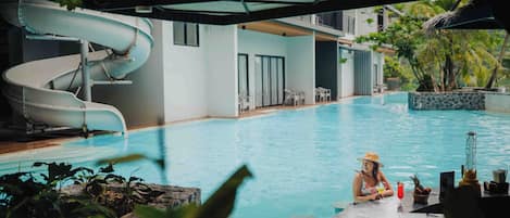 A pool with a water slide, lounge chairs, and a tropical setting.