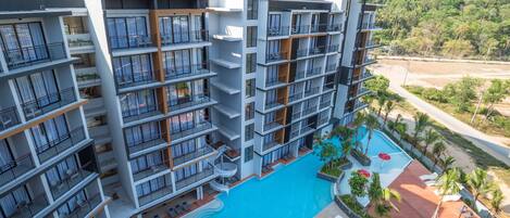 A multi-story hotel with balconies, a swimming pool, and a view of a mountainous landscape.