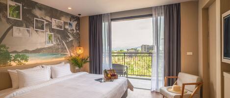 Habitación de hotel con una cama grande, una silla, un balcón con vista a la ciudad y un cuadro con imágenes enmarcadas.