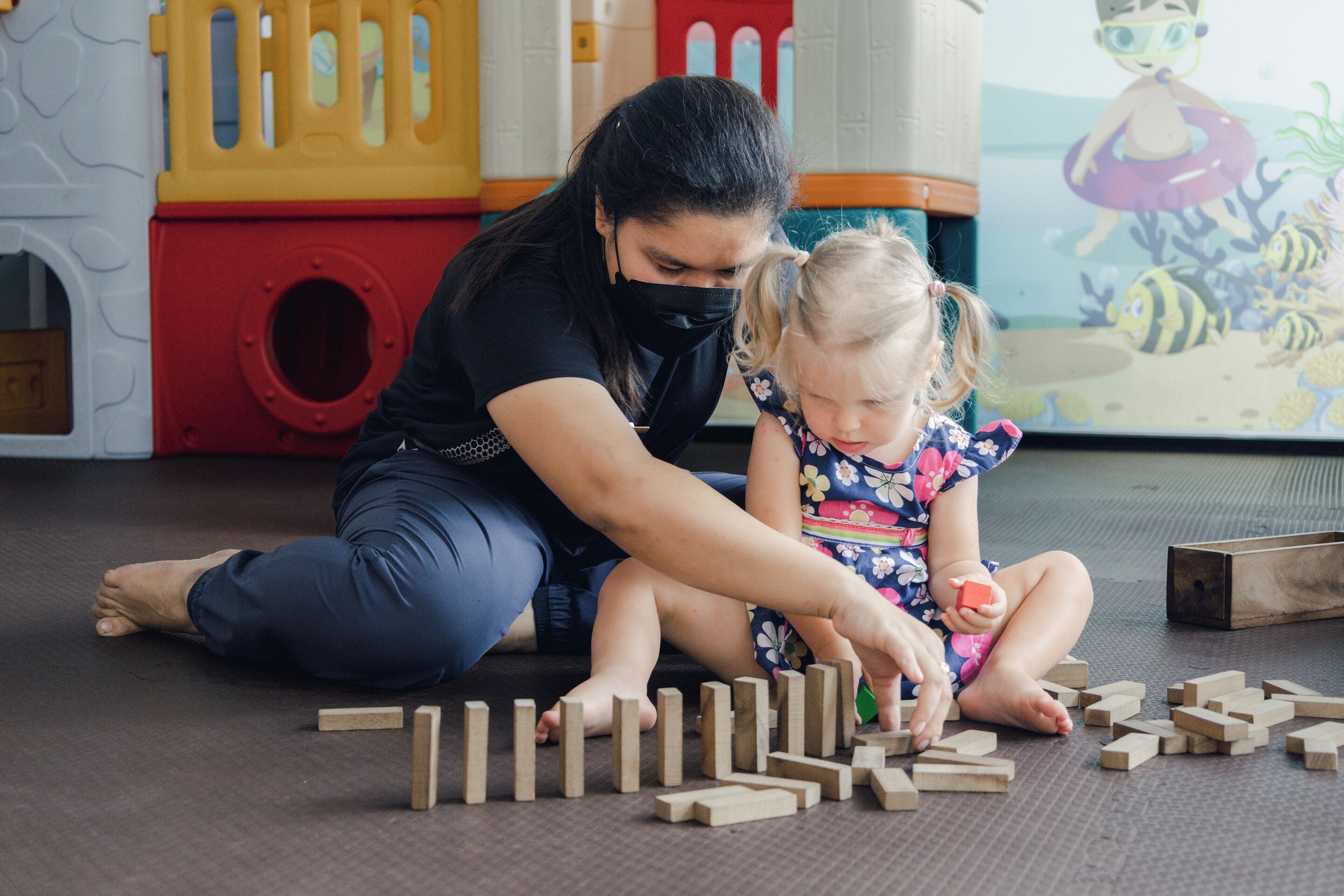 Une femme et un enfant jouent avec des blocs de bois sur un tapis.