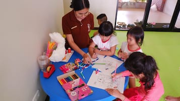A group of children and an adult engaged in a drawing activity at a round table with art supplies.