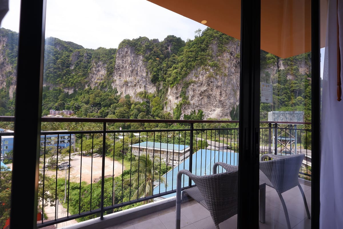 Un balcon donnant sur un paysage montagneux, une piscine et un bâtiment avec un toit bleu.
