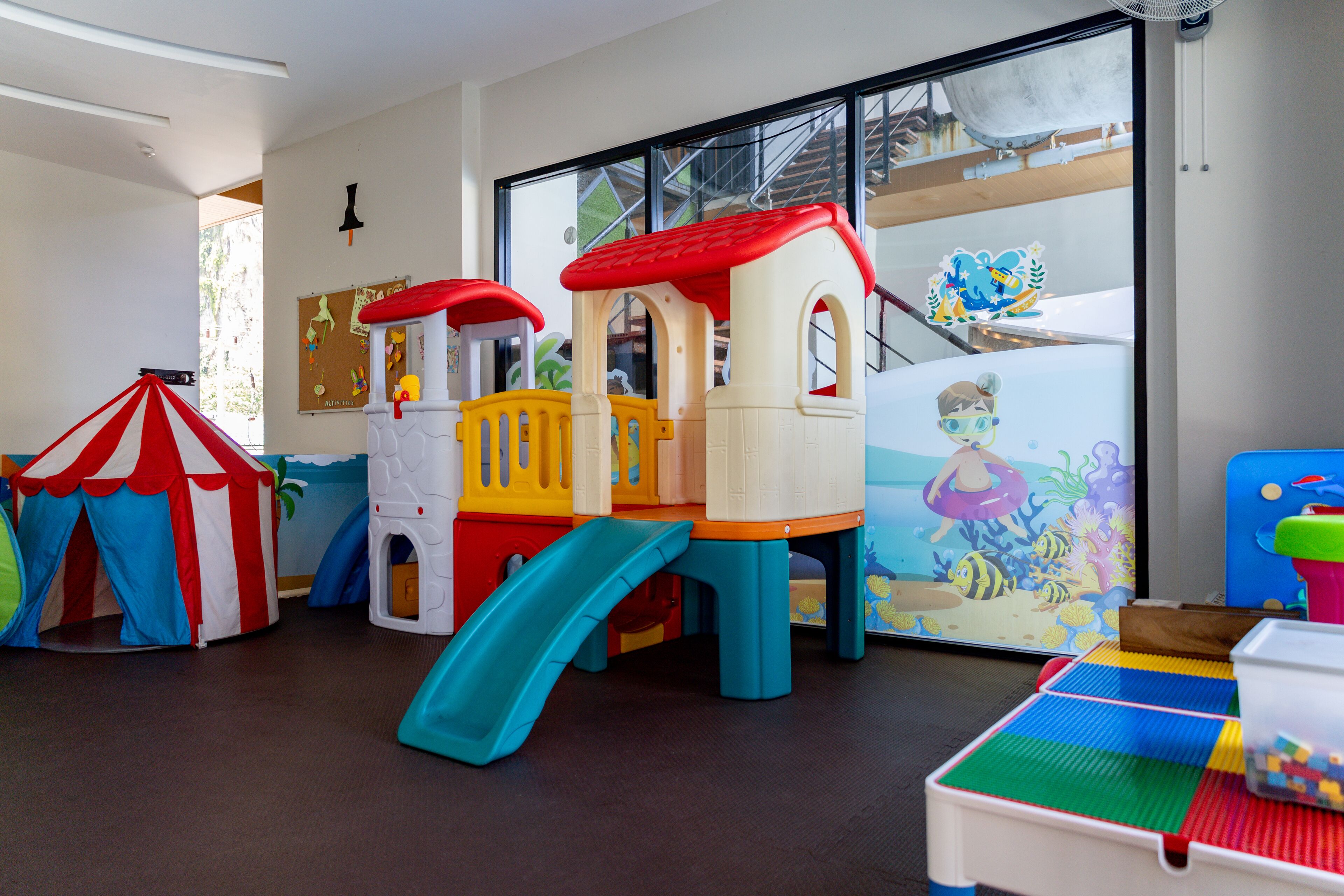 Zona de juegos infantiles con un tobogán, una casita y una tienda de campaña.