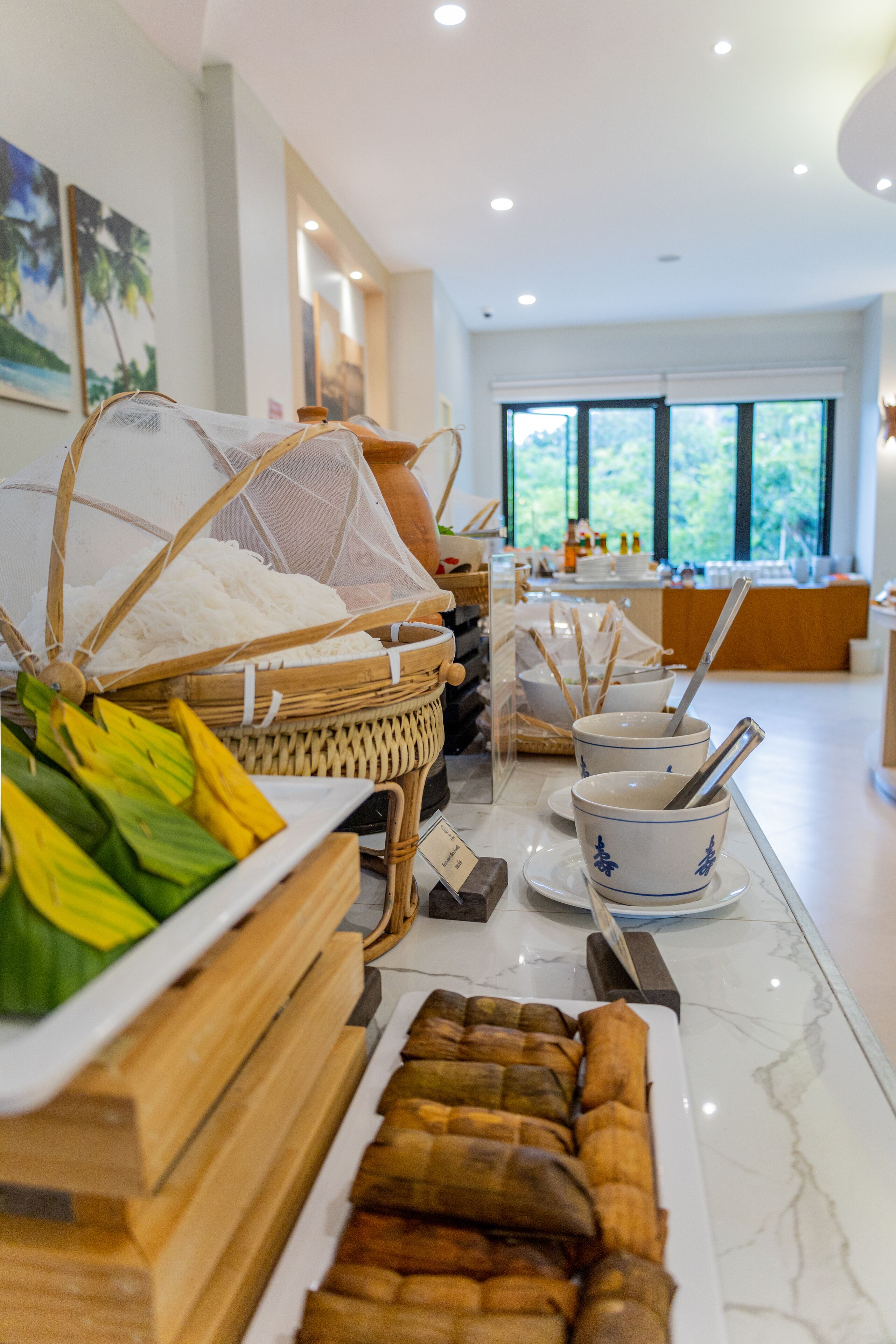A buffet setup with various food items and utensils, including a basket of rice and a tray of wrapped items.