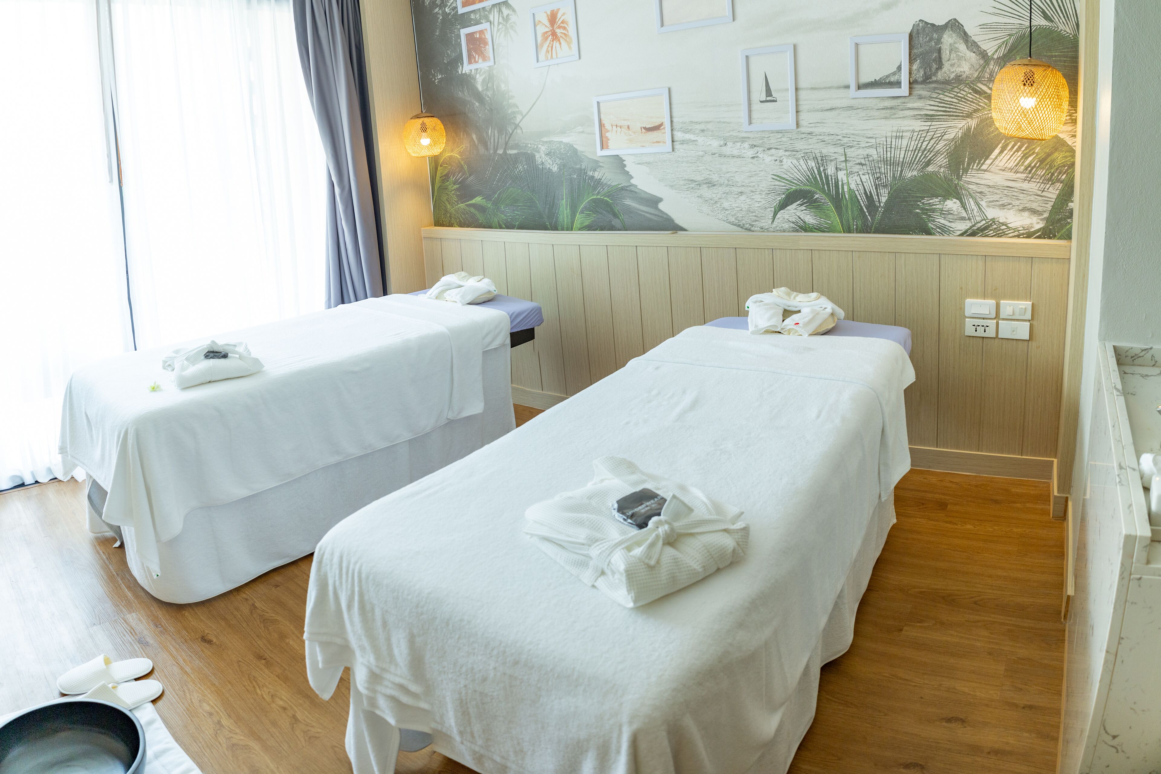 A room with two beds, each with a white bedspread and a towel. There is a wall mural depicting a beach scene.