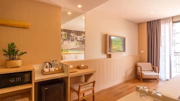 Una habitación de hotel moderna con un escritorio de madera, un refrigerador pequeño, una silla cómoda, una cama y un espejo grande.