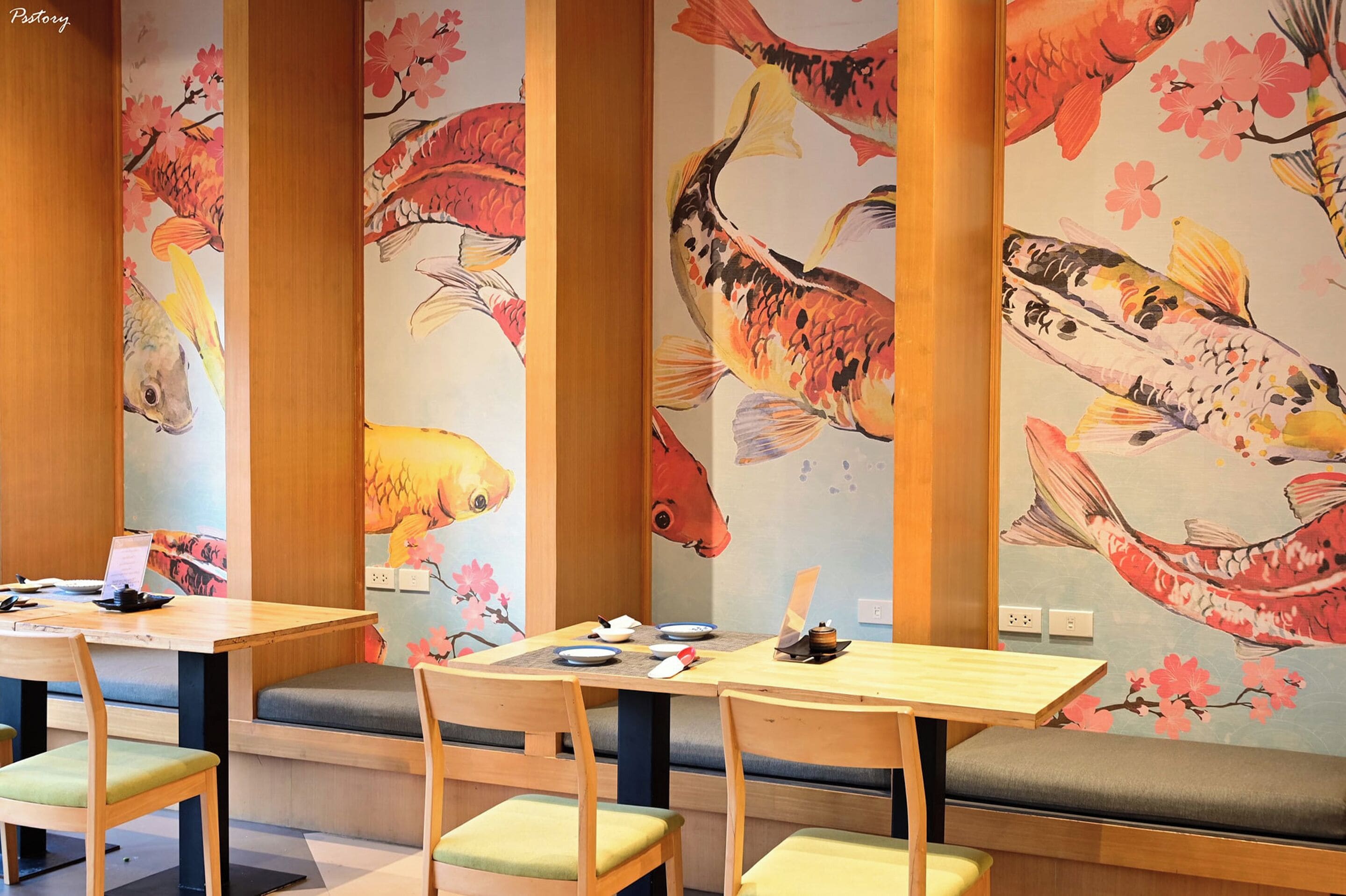 Un restaurante con mesas y bancos de madera, decorado con murales de carpas y flores de cerezo en las paredes.