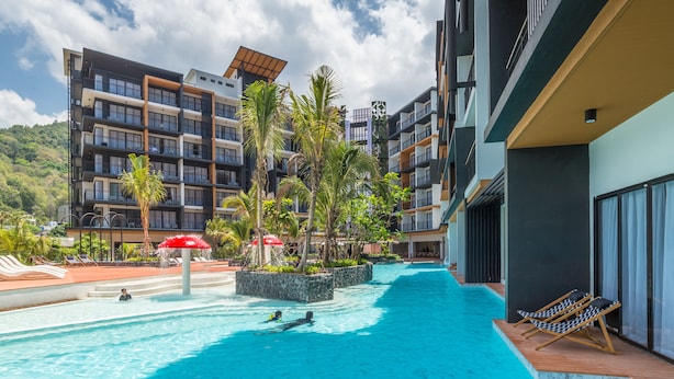 Una piscina con sillas de descanso, palmeras y un edificio moderno con balcones.