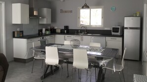 A modern kitchen with white cabinets, a dining table with chairs, a window with a view, and a refrigerator. - Bassin d'arcachon, a cozy little nest between dune du pyla and cap-ferret  (Audenge)