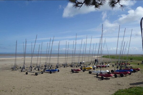 A sandy beach with numerous sailboats and small motorboats lined up.