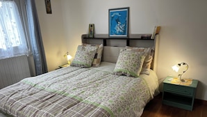 Una cama bien hecha con ropa de cama floral, una lámpara de noche y una mesita de noche pequeña con lámpara.