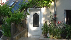 Una casa blanca con tejado azul, cerca de madera y un pequeño jardín con flores y plantas.