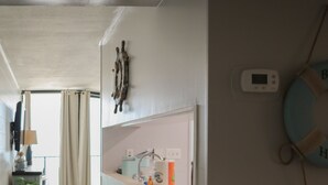 Un pasillo con suelo de madera, una pared blanca con un estante que sostiene artículos de aseo, un termostato fijado a la pared y un adorno de salvavidas.