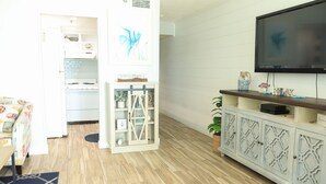 Una sala de estar con televisor, armarios de madera, una cocina al fondo y un tapete estampado.