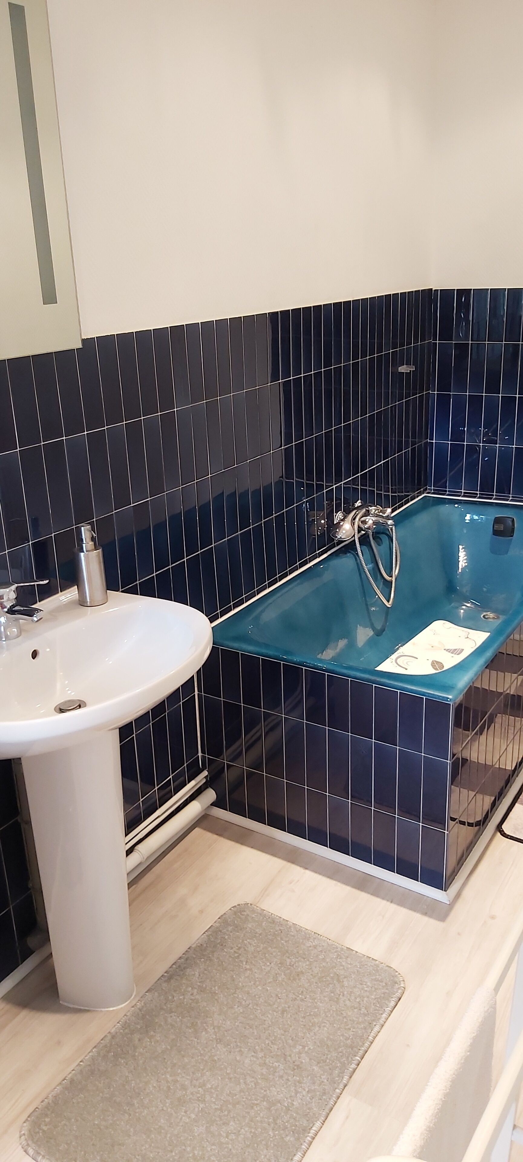 Une salle de bain avec un lavabo blanc, une baignoire bleue et des murs recouverts de carreaux bleu foncé.