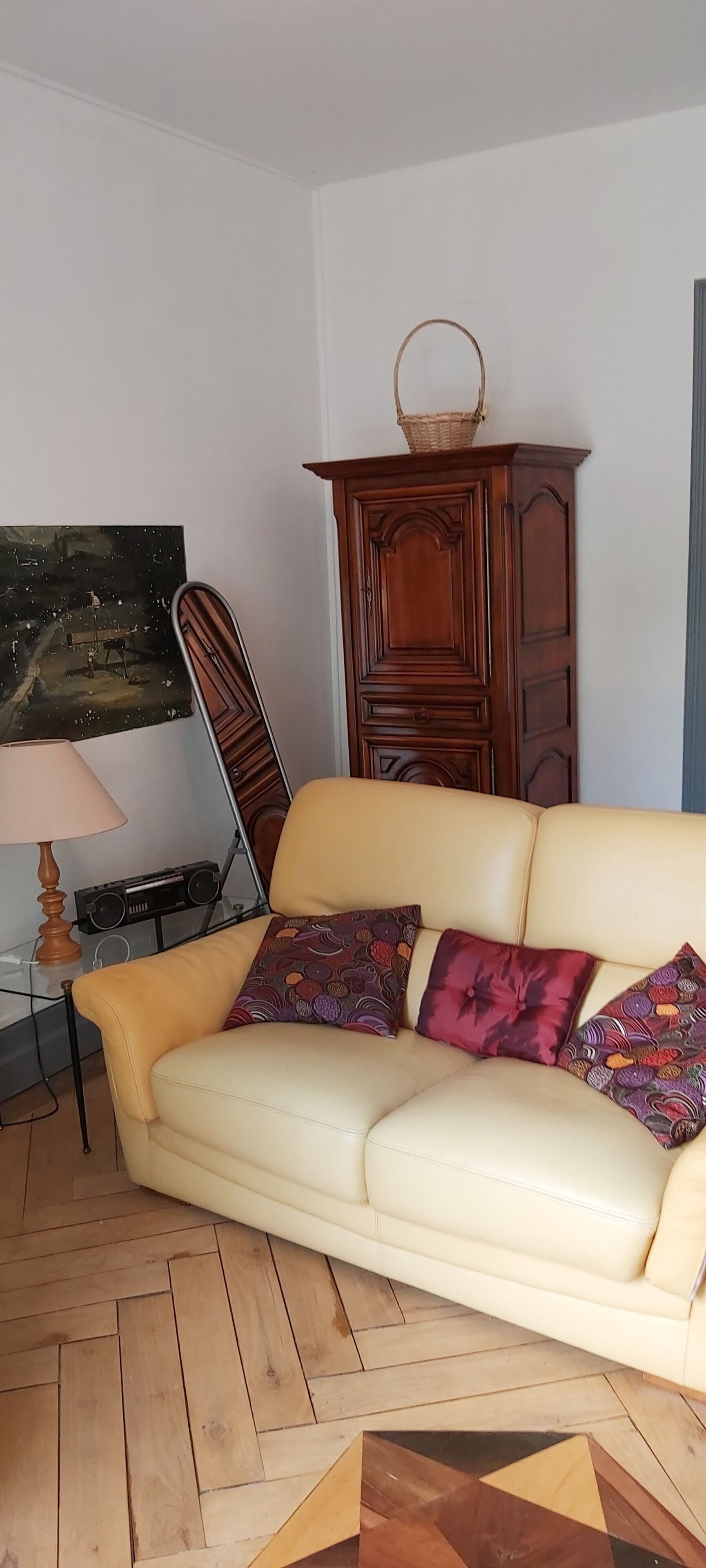 Un salon avec un canapé beige, des coussins à motifs, un meuble en bois, une radio et une lampe.