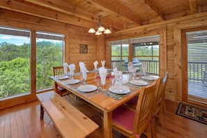 Enjoy meals in this dining room with a large table, exposed beams, and a view of the surrounding greenery.