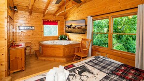 A log cabin room with a wooden interior, a large window, a painting, a ceiling fan, and a wooden chair. - A+ Views & Location! > Parkway, Dollywood. Theater, Hot Tub, Games, Pet Friendly (Pigeon Forge)