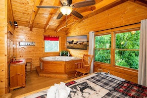 A log cabin room with a wooden interior, a large window, a painting, a ceiling fan, and a wooden chair. - A+ Views & Location! > Parkway, Dollywood. Theater, Hot Tub, Games, Pet Friendly (Pigeon Forge)