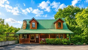 A log cabin with a green metal roof, a stone chimney, and a porch with a railing. - A+ Views & Location! > Parkway, Dollywood. Theater, Hot Tub, Games, Pet Friendly (Pigeon Forge)