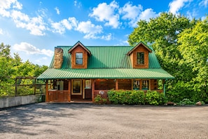 A log cabin with a green metal roof, a stone chimney, and a porch with a railing. - A+ Views & Location! > Parkway, Dollywood. Theater, Hot Tub, Games, Pet Friendly (Pigeon Forge)