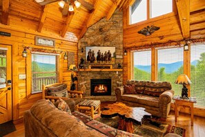 A log cabin interior with a fireplace, wooden furniture, and a stone wall. - A+ Views & Location! > Parkway, Dollywood. Theater, Hot Tub, Games, Pet Friendly (Pigeon Forge)