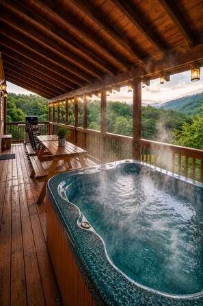 Un bain à remous sur une terrasse en bois, avec vue sur une chaîne de montagnes boisées.