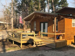 A wooden cabin with a porch, outdoor seating, and a flag. - WATERFRONT CABIN #3 Lake Livingston, Onalaska, Texas (Onalaska)