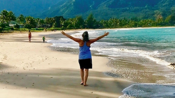 Ein Strand mit einer Person, die die Arme hebt und auf ein Gebirge blickt.