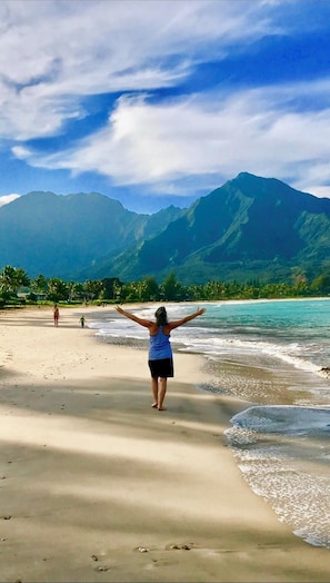 Ein Strand mit einer Person, die die Arme hebt und auf ein Gebirge blickt.