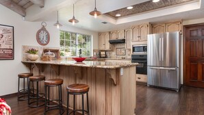 Una cocina con alacenas de madera, un refrigerador de acero inoxidable, un microondas y una isla grande con taburetes.