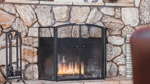 Una chimenea de piedra con un cuadro enmarcado de un caballo sobre ella, un mosquitero negro y un cofre de madera al frente.