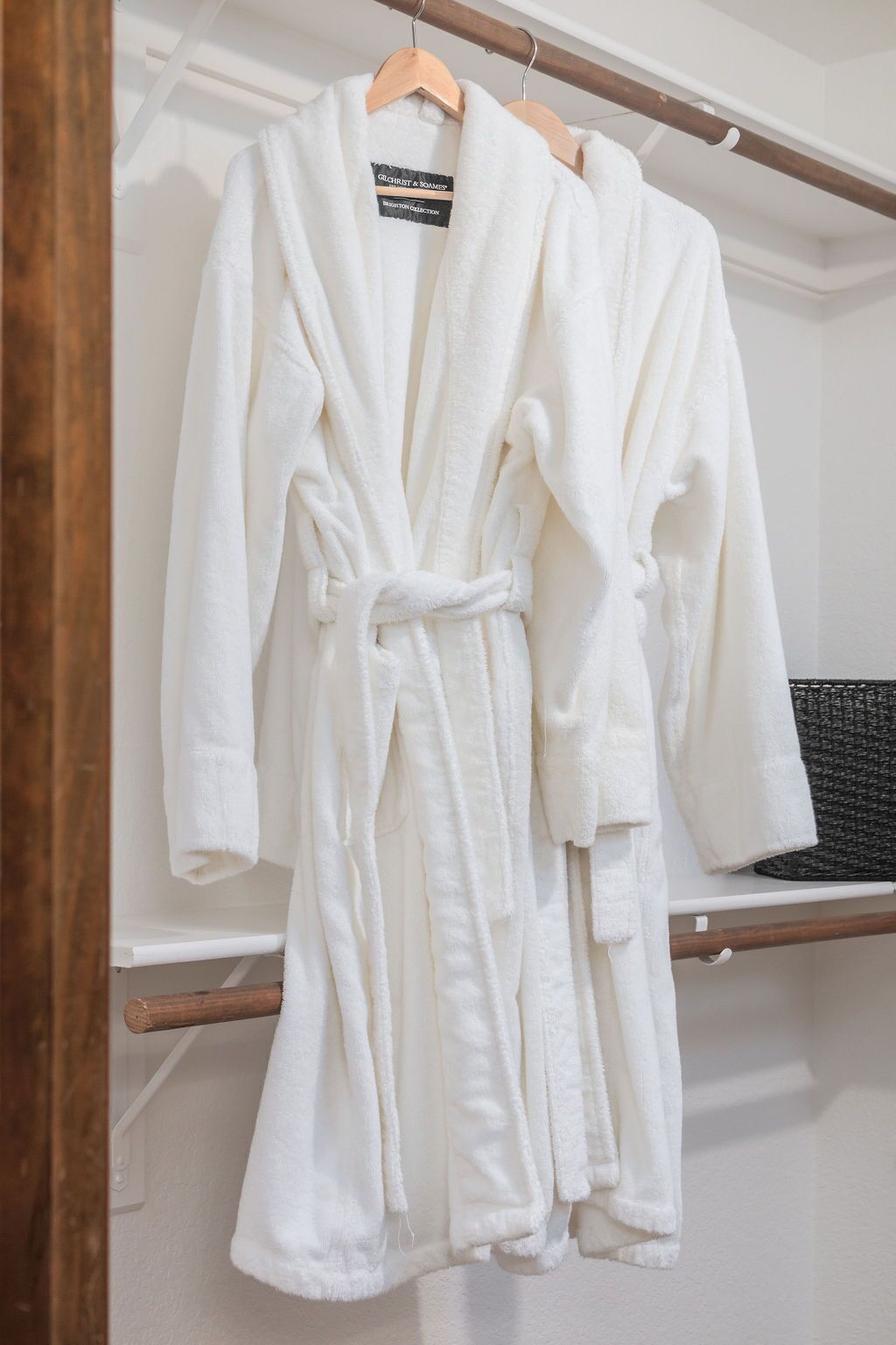 A white bathrobe hanging on a wooden hanger in a white room.