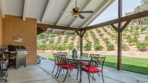 Un patio cubierto con mesa y sillas, una parrilla y vistas a un viñedo.