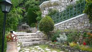 Una escalera de piedra que asciende hacia un muro de piedra, rodeada de vegetación exuberante y diversas flores.