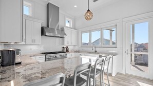 A modern kitchen with white cabinets, a large island with bar stools, a stainless steel stove, and a view through the glass door. - Lake Front w/ Dock, Kayaks and Pool (Santa Rosa Beach)