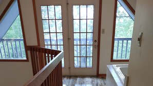 Un hall d’entrée spacieux, doté d’un plancher en bois, d’une rambarde en bois et de grandes fenêtres offrant une vue sur un balcon et sur la verdure.