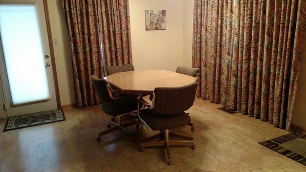 A dining room with a wooden table and four chairs, patterned curtains, and a small rug on the floor.