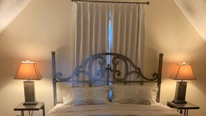 Une chambre à coucher comprenant un lit, deux tables de chevet avec des lampes, une tête de lit décorative et une fenêtre avec des rideaux.