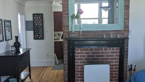 Un salon avec une cheminée en briques, un canapé bleu, un plancher en bois et un coin repas avec une table et des chaises en bois foncé.