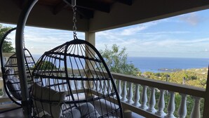 Een hangstoel met kussens op een balkon met uitzicht op zee.
