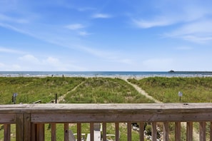A wooden deck with a view of the beach and a pier in the distance.