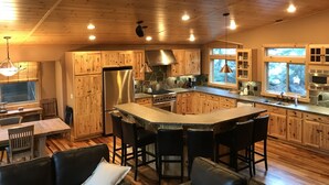 Una cocina amplia con armarios de madera, un refrigerador de acero inoxidable, una isla grande con taburetes de bar y un protector contra salpicaduras de piedra.