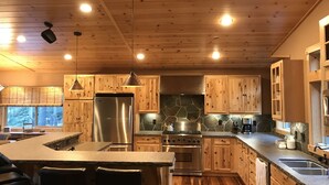 Una cocina moderna con armarios de madera, un refrigerador de acero inoxidable, una estufa y una isla grande con taburetes de bar.