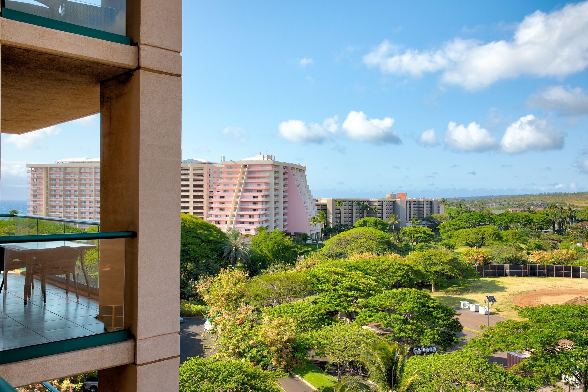 A high-rise building with multiple balconies, lush greenery, and a clear sky.