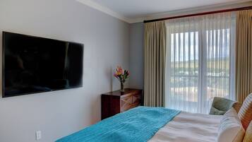 A bedroom with a bed, a TV mounted on the wall, a dresser, and a window with curtains.