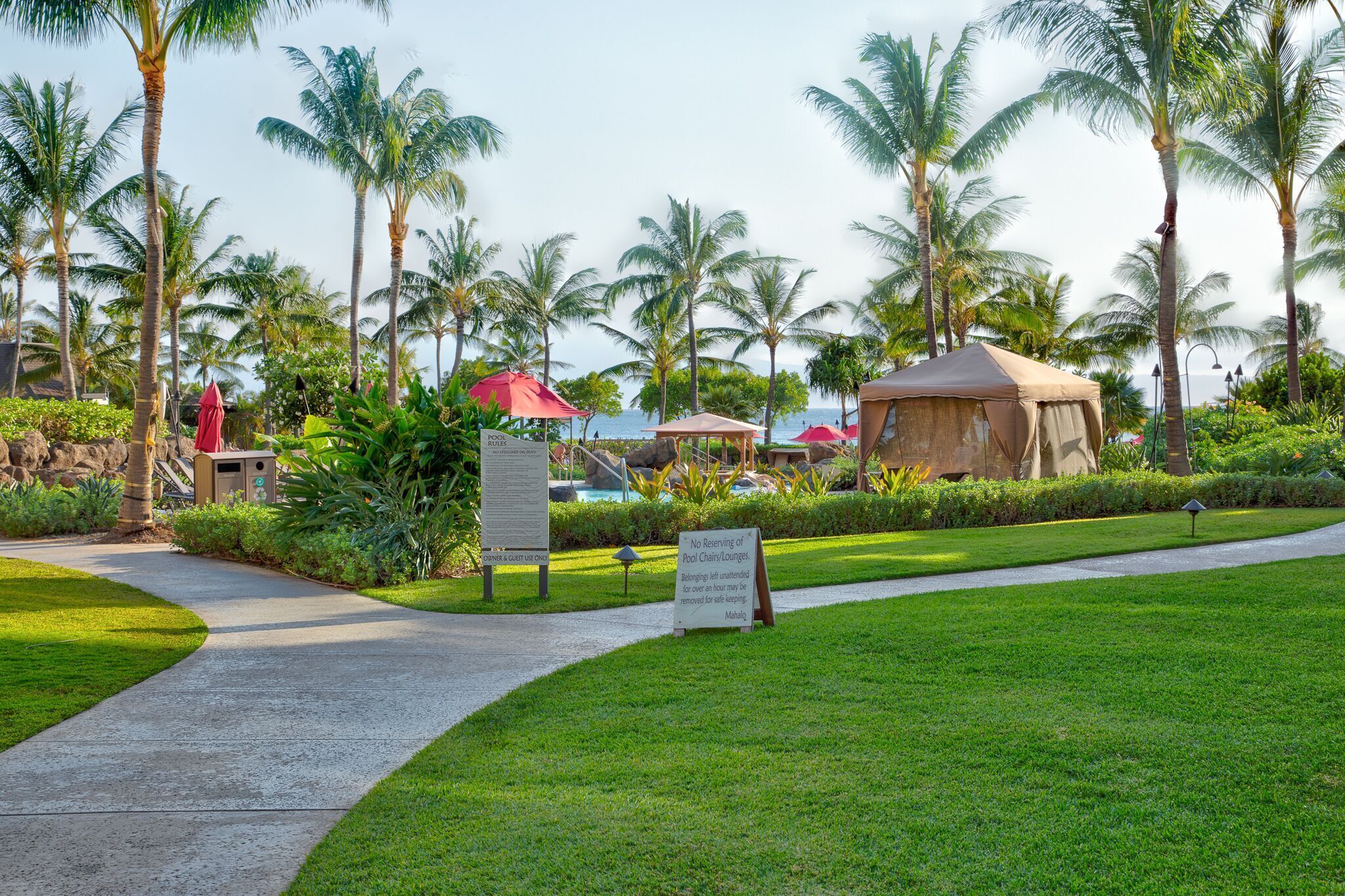A resort with a pool area, palm trees, and a sign indicating no reservation of pool chairs/lounges.